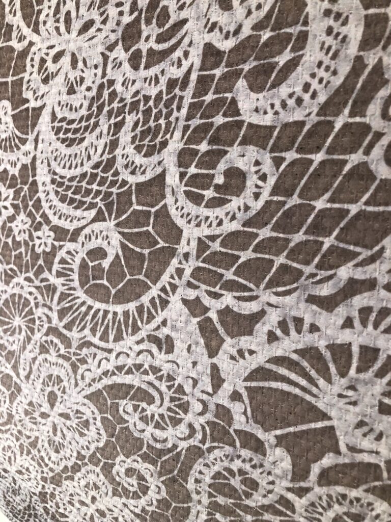 Primo piano di rivestimento murale con texture effetto pizzo bianco su sfondo marrone