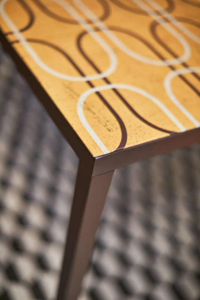 Dettaglio piano tavolo Momenti arancione con pattern circolare su struttura metallica